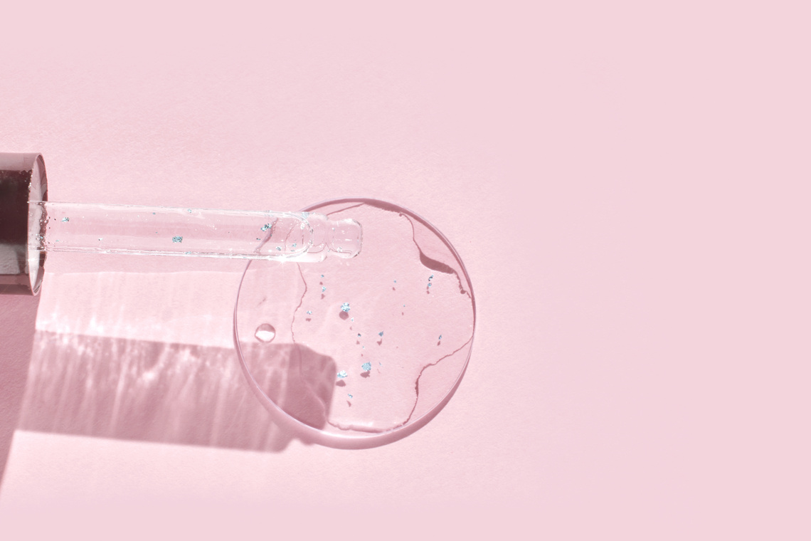 Serum gel texture swatch. Transparent drop with golden sparkles. Pink background